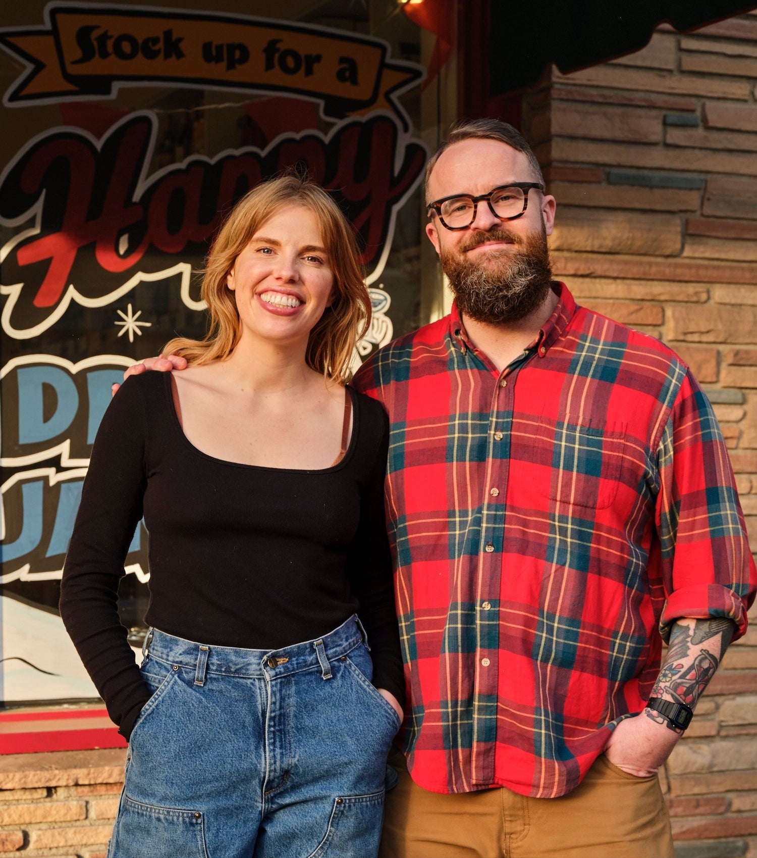 Two people standing together in front of a building with a sign.